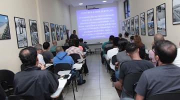 Homens estão sentados em sala de aula. #Paratodosverem