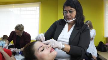 mulher faz a sobrancelha de outra sentada #paratodosverem