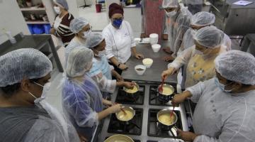 pessoas de pé mexendo em panelas sobre fogão industrial. Trata-se de uma aula de culinária. #paratodosverem