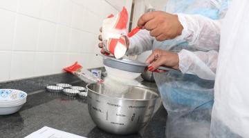 foto em close de mãos coando farinha em pote de alumínio para preparar alimento. #paratodosverem