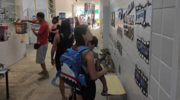 adultos olham fotos afixadas em parede de escola. #paratodosverem 