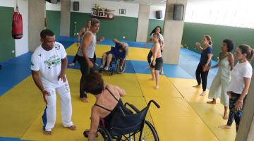 Cadeirantes e mulheres em pé realizam atividade. #paratodosverem