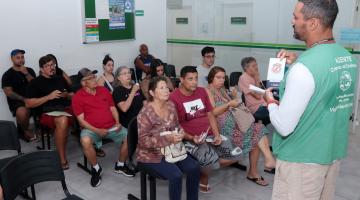 agente fala com pessoas sentadas na sala de espera #paratodosverem