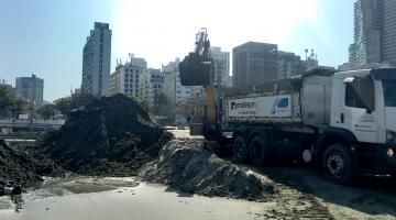 caminhão está parado na faixa de areia e escavadeira ao fundo remove volume de areia de dentro do canal. #paratodosverem