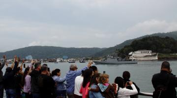 Público tira fotografias de navio militar em passagem pela Fortaleza da Barra no canal do Estuário. #paratodosverem