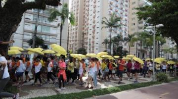 pessoas caminham no calçadão da orla com guarda-chuvas amarelos. #paratodosverem