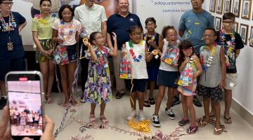 crianças usando óculos posam para foto com alguns adultos. O ambiente está decorado com itens de carnaval. #paratodosverem