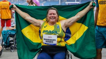 a atleta de braços aberto segurando a Bandeira do Brasil. #paratodosverem