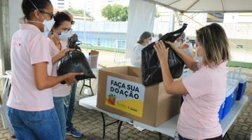 Mulheres colocam doação em caixa de papelão no posto de vacinação #paratodosverem
