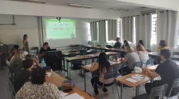 sala de aula com adultos sentados assistindo a uma mulher que fala à frente de todos e diante de uma tela onde estão projetadas imagens sobre doação de órgãos. #paratodosverem