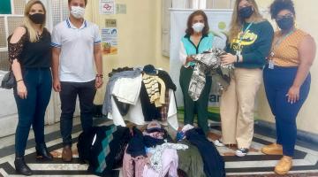 roupas dentro de caixas no chão. Cinco pessoas posam para foto atrás das caixas. #paratodosverem