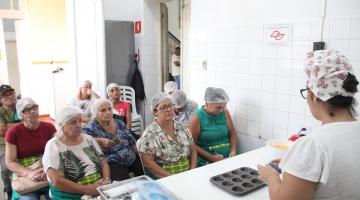 professora prepara doce enquanto é observada por alunas #paratodosverem 