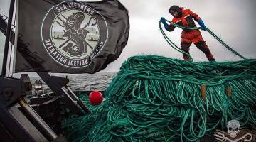 cena do documentário. Homem está em cima de barco, puxando uma imensa corda. Ao lado dele, uma bandeira da Sea Shepperd. #paratodosverem