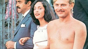 Mulher caminha com dois homens na rua. O da direita está vestido de terno. O da esquerda está nu. #paratodosverem