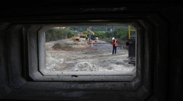 fotógrafo se posicionou na entrada de aduela para fazer dela uma moldura e mostrar a sua proporção em relaão ao homem e máquinas que estão no fundo. #paratodosverem