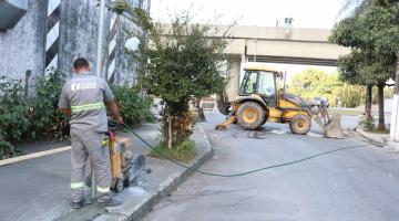 Profissional trabalha em obra de sarjeta com retroescavadeira ao fundo. #pratodosverem