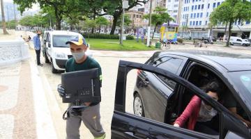 Homem carrega monitora doado por mulher dentro de veículo preto. #pracegover