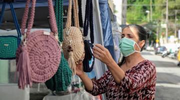 Mulher mexe em bolsas de crochê em uma barraca #paratodosverem