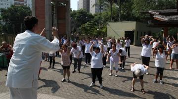 aula de tai chi chuan com professor de costas para imagem fazendo movimento que é repetido pelos alunos à frente. #paratodosverem 