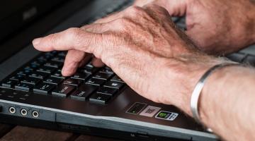 mãos de pessoa idosa digitando em computador. #paratodosverem 