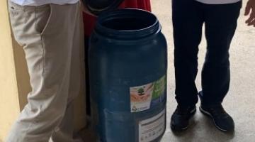 dois homens em pé ladeiam tonel para depósito de óleo de cozinha usado. #paratodosverem