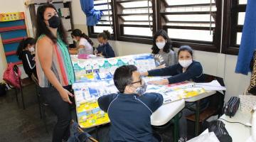 Professora e alunos na sala confeccionando cobertor com caixas de leite #paratodosverem