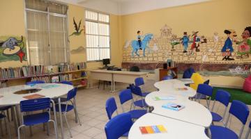 Interior de classe com pintura artística nas paredes. Mesas e cadeiras. #paratodosverem