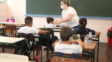Sala de aula com professora à frente dos alunos sentados em suas carteiras. #Paratodosverem
