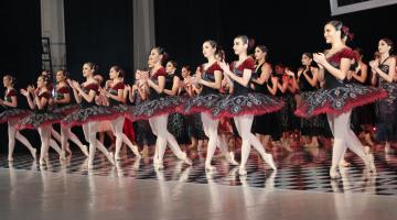 Bailarinas estão em pé enfileiradas no palco. Elas batem palmas. #Pracegover