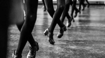 Close em pés de bailarinas de sapateado. Todos estão cruzados e no ar. #Pracegover