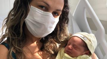 Mulher usando máscara com bebê no colo. #Paratodosverem
