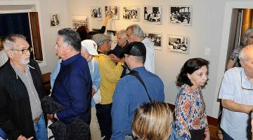 público está em uma sala conversando o observando imagens afixadas em parede. #paratodosverem 