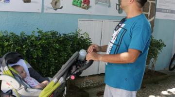 Homem com bebê ao lado em carrinho olha fotos da exposição. #pracegover