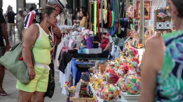 bancas com artesanatos expostos e público olhando. #paratodosverem 