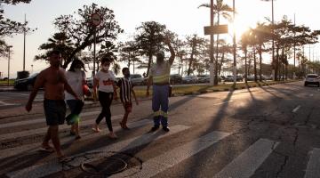 agente da CET está sobre a faixa e faz sinal para veículos. Pessoas atravessam a rua. #paratodosverem