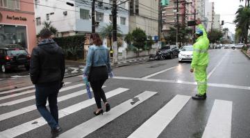 Agente sinaliza para motorista parar carro, enquanto pedestres atravessam na faixa. #pracegover