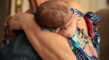 Imagem em close de bebê no colo de uma mulher. #paratodosverem