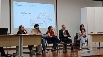 cinco pessoas sentadas diante de mesa e à frente de telão. #paratodosverem