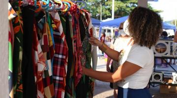 mulher mexe em roupas penduradas em arara em local aberto. #paratodosverem