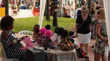 Pessoas observam barraca com bonecas afro #paratodosverem