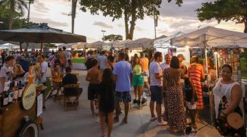 pessoas circulam em praça onde estão montadas barracas com exposição de peças artesanais. #paratodosverem