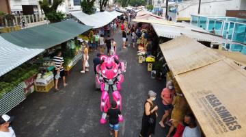 ROBO ESTÁ NO MEIO DA RUA, ENTRE AS BARRACA, INTERAGINDO COM CRIANÇA. hÁ PESSOAS CIRCULANDO PELA FEIRA. #PARAOTDOSVEREM