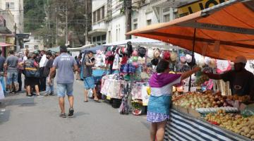 Feira está armada em rua. Pessoas estão andando na rua ou paradas em frente a barracas. #Paratodosverem