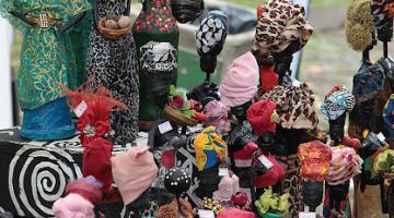 Bonecas negras com roupas afros coloridas em estande da feira. #pratodosverem