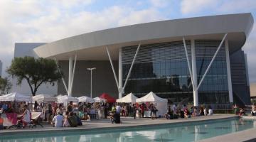 Foto da fachada do Santos Convention Center com várias barraquinhas e pessoas na frente. #paratodosverem