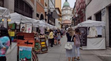 Quadros e outros produtos artesanais em barracas de boulevard, com a Bolsa do Café ao fundo. #pracegover