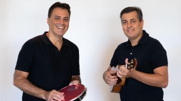 dois homens estão lado a lado. Um toca pandeiro e o outro, cavaquinho