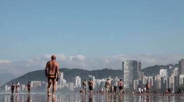 Pessoas andando na beira da água em praia de Santos #paratodosverem