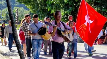 pessoas andando segurando bandeira e tocando instrumentos #paratodosverem