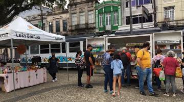 Pessoas na praça olhando estandes com livros #paratodosverem